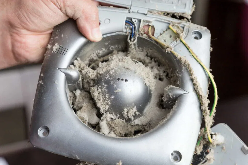 Close-up of a technician's hands holding a heavily dusty silver exhaust fan during a professional ventilation cleaning service in Ocala, Florida.