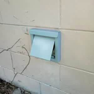 A newly installed blue-grey DryerWallVent mounted securely on a concrete block wall, featuring a clean, low-profile design and a functional gravity-assist damper.